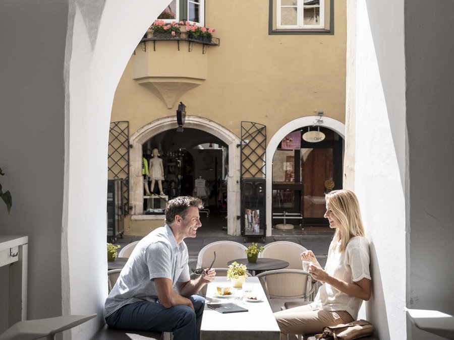 Süße Boutiquen, edle Delikatessengeschäfte Paar sitzt und unterhält sich in einem Café mit gelber Hausfassade im Hintergrund