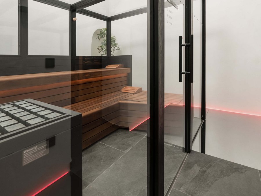 Benessere all’Aquila Nera Sala sauna moderna con pareti di vetro, panche in legno e illuminazione LED rossa