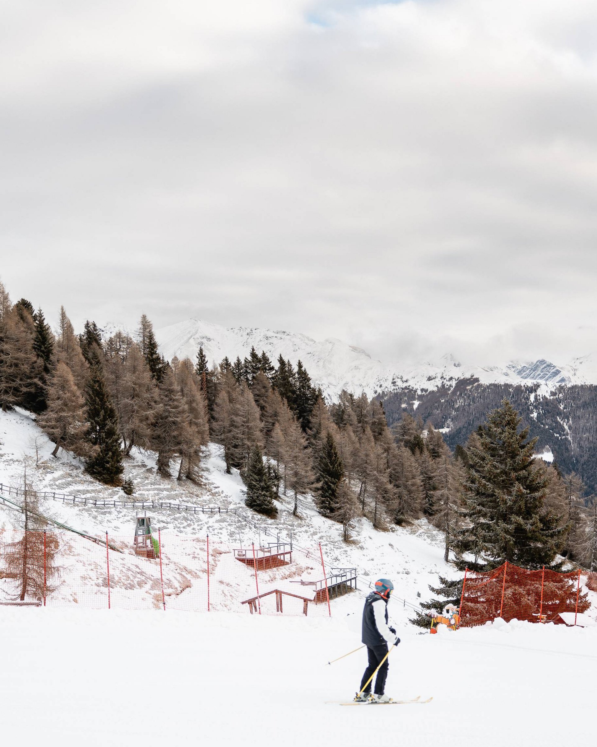 Skifahrer auf einer schneebedeckten Piste vor bewaldetem Berghang