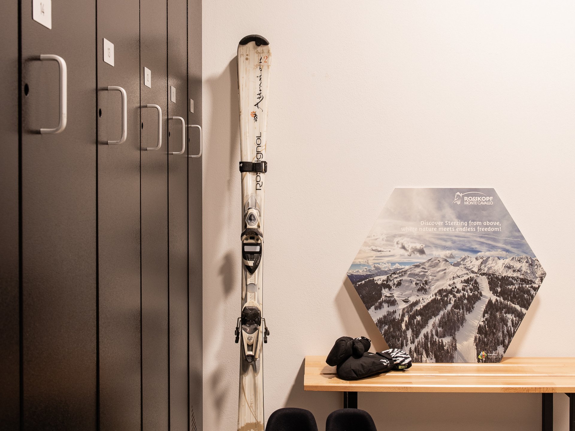 Ski boots, skis, and gloves next to lockers and bench in changing room