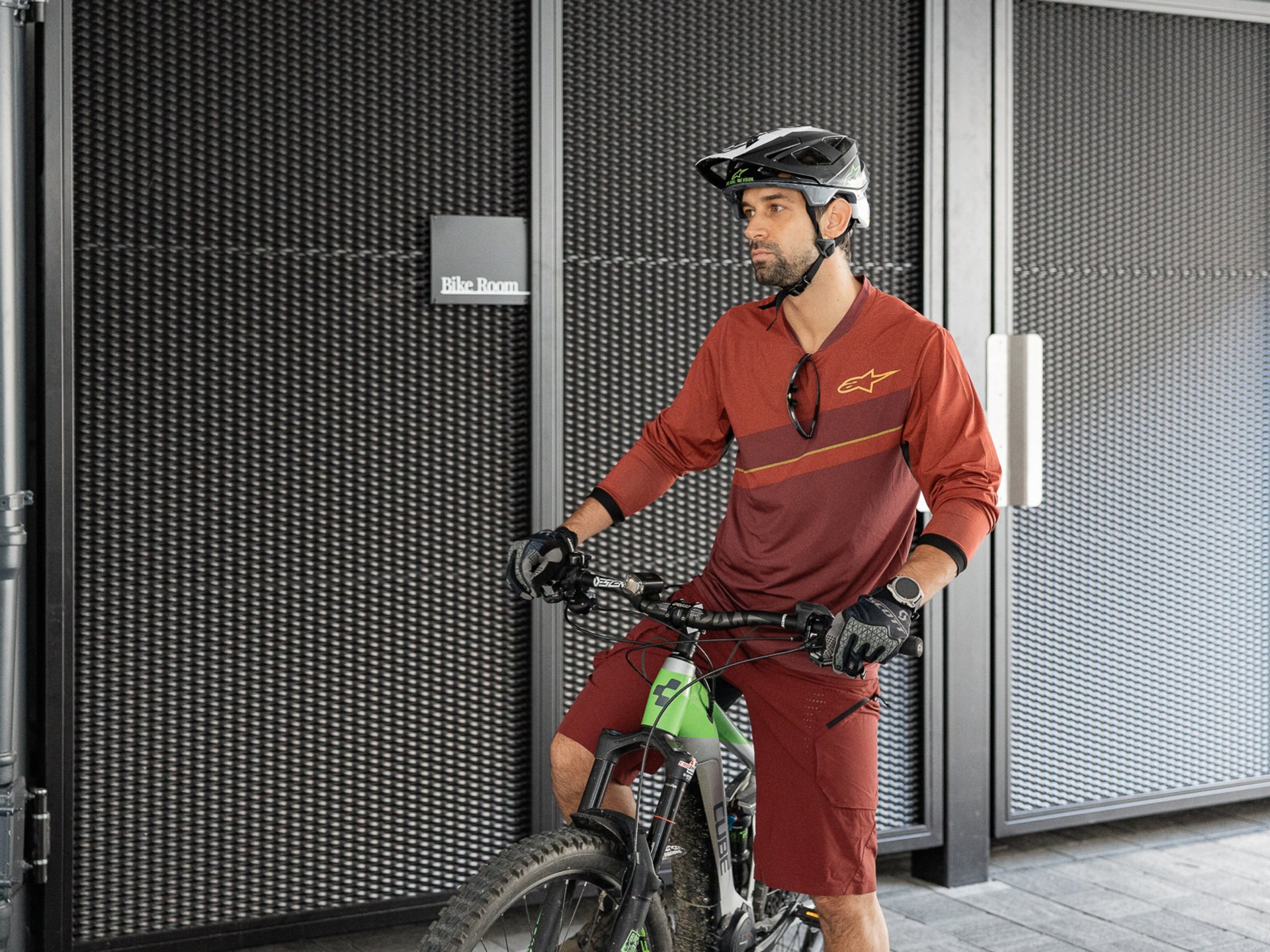 Man with helmet standing with mountain bike in front of bike room entrance