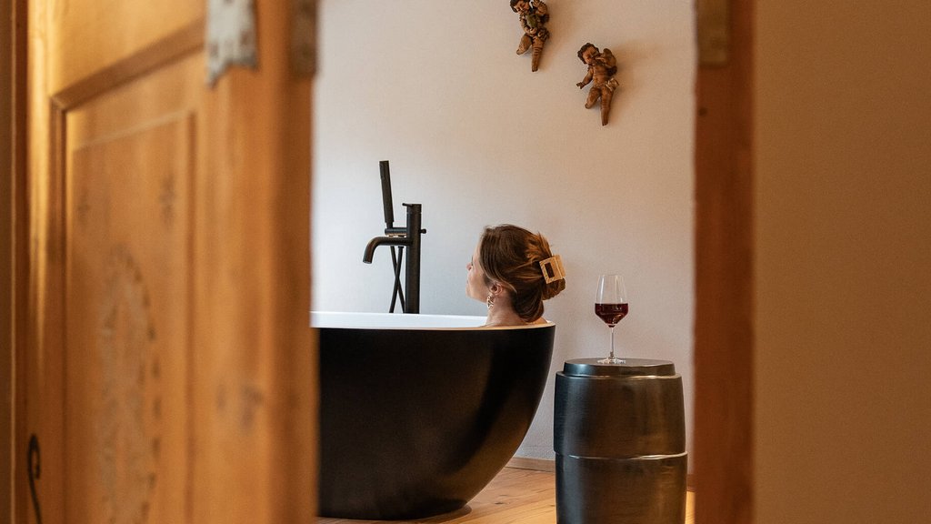 Frau entspannt in schwarzer Badewanne, mit Weinglas auf Hocker, gesehen durch Tür