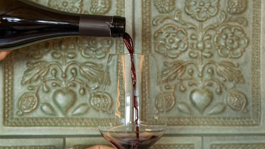 Roter Wein wird aus einer Flasche in ein Weinglas gegossen vor grüner Wand