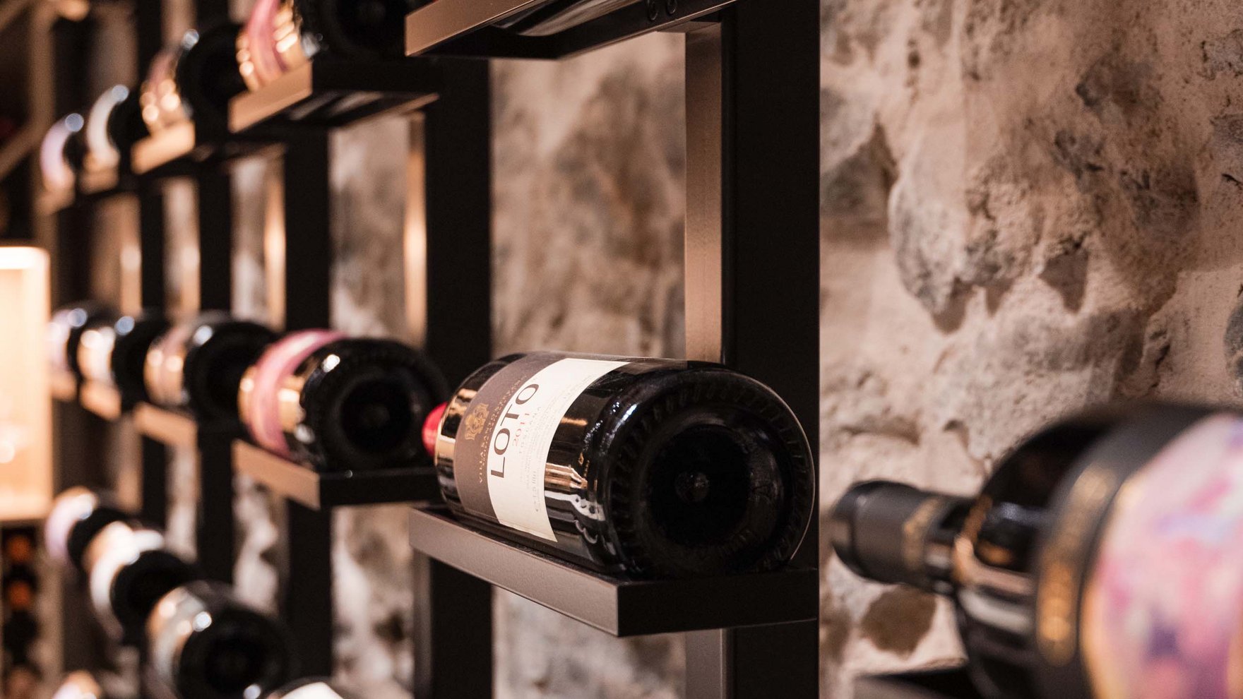 Wine bottles on metal racks against a stone wall