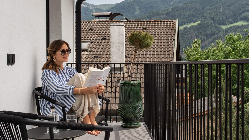 Frau liest entspannt auf Balkon mit Bergblick