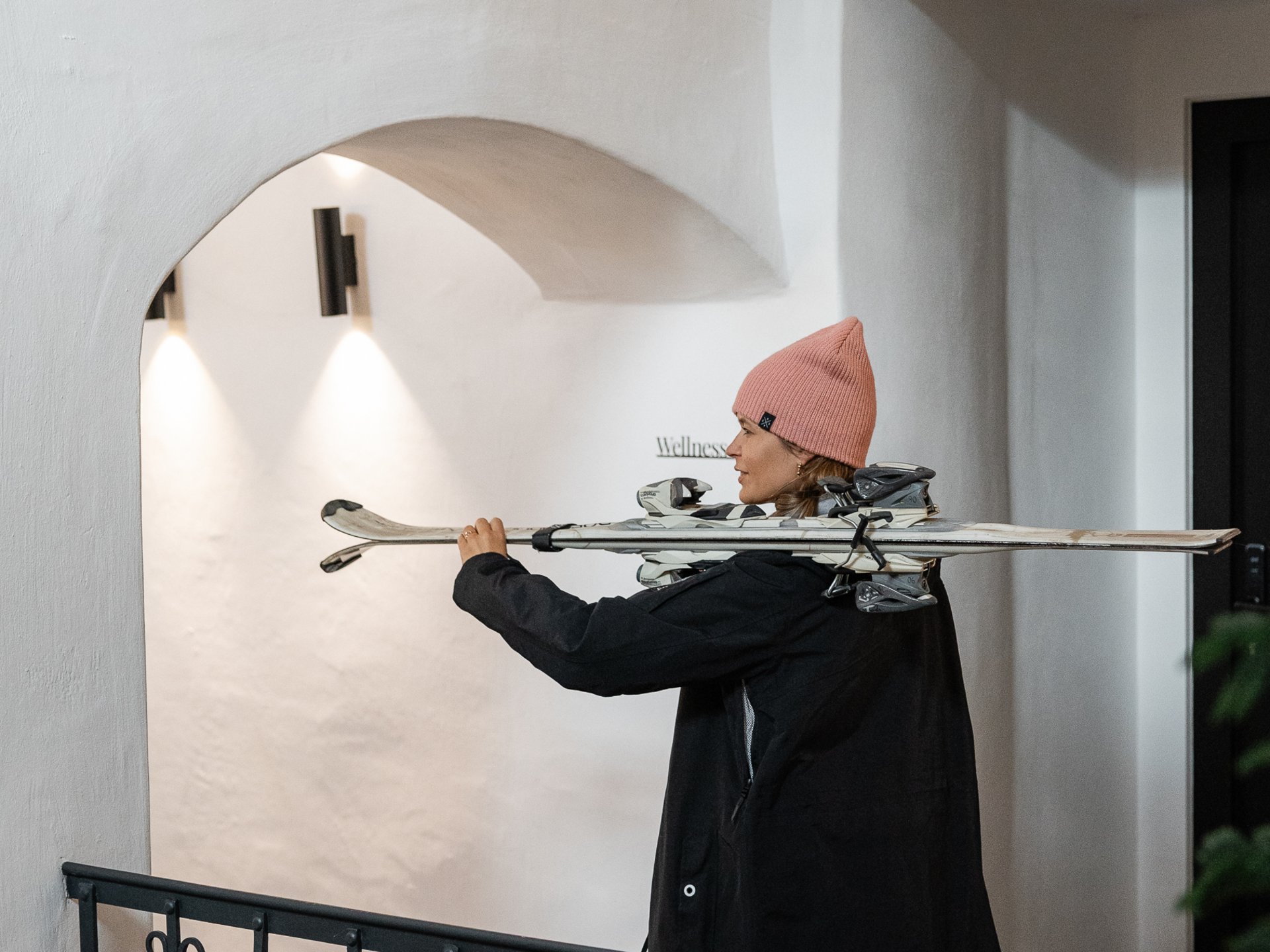 Woman carrying skis walking inside a building with white walls