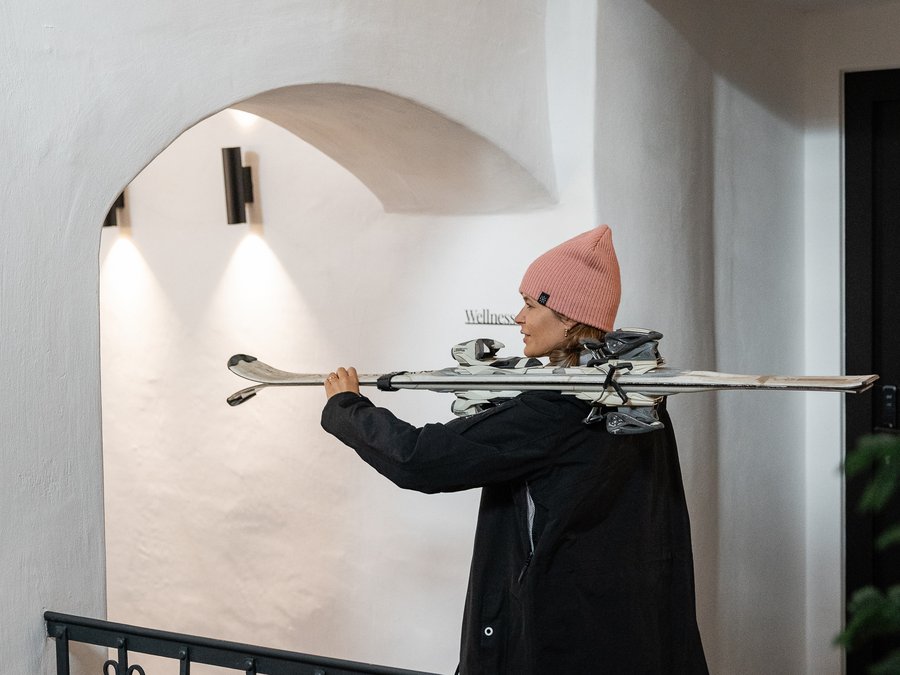 Discover the Schwarzer Adler Woman carrying skis walking inside a building with white walls