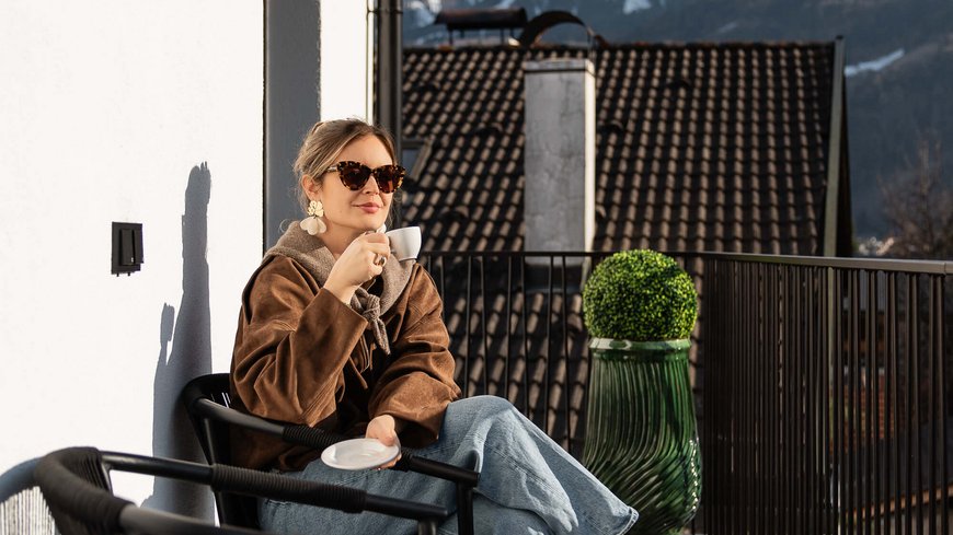 Die perfekte Location für euer Apartment in Sterzing Frau trinkt Kaffee auf Balkon mit Bergblick bei sonnigem Wetter