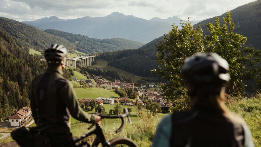 Cooles Rennradhotel in Südtirol Zwei Radfahrer blicken auf ein Tal mit Brücke und Bergen im Hintergrund
