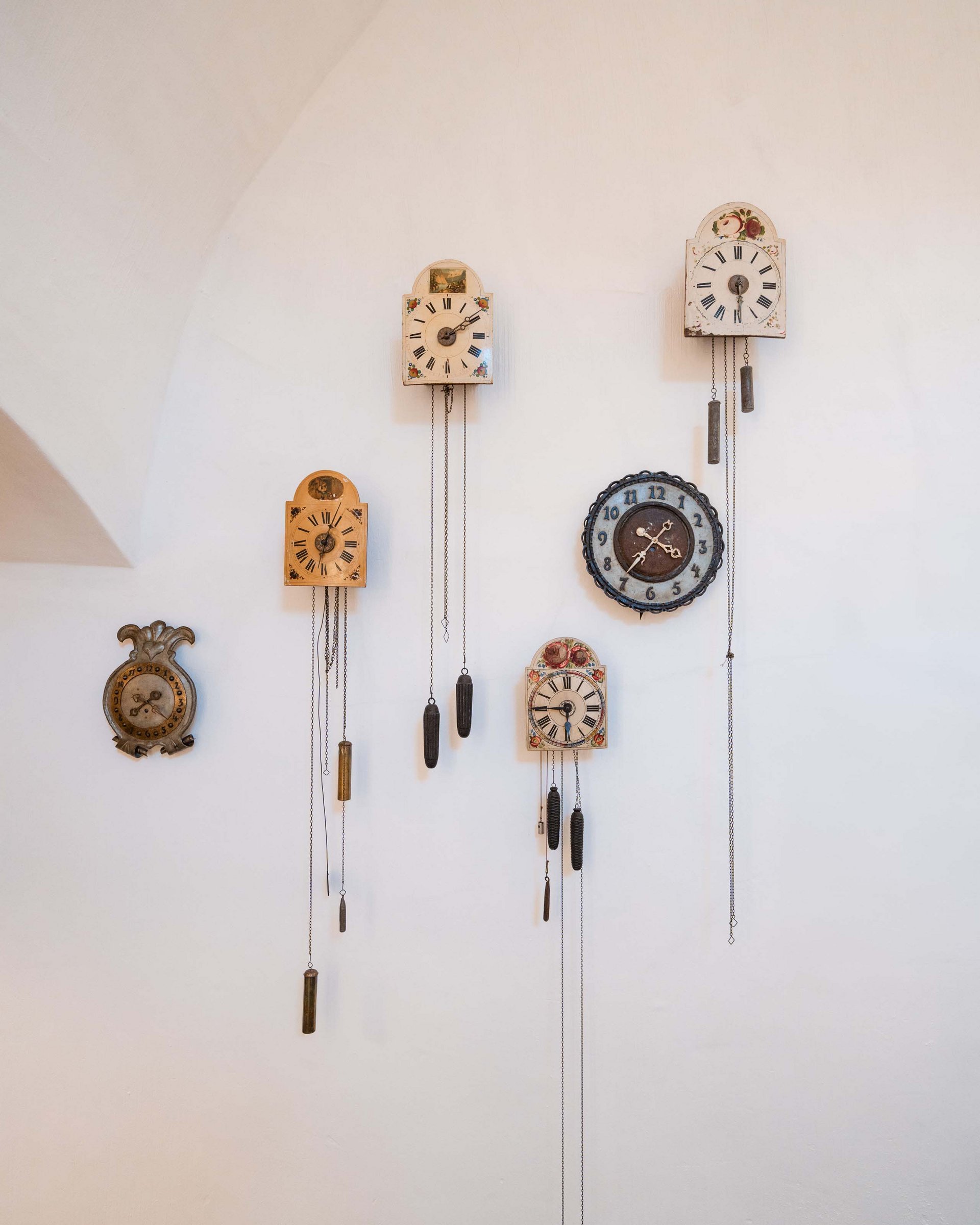 Antique wall clocks with weights hanging on a white wall