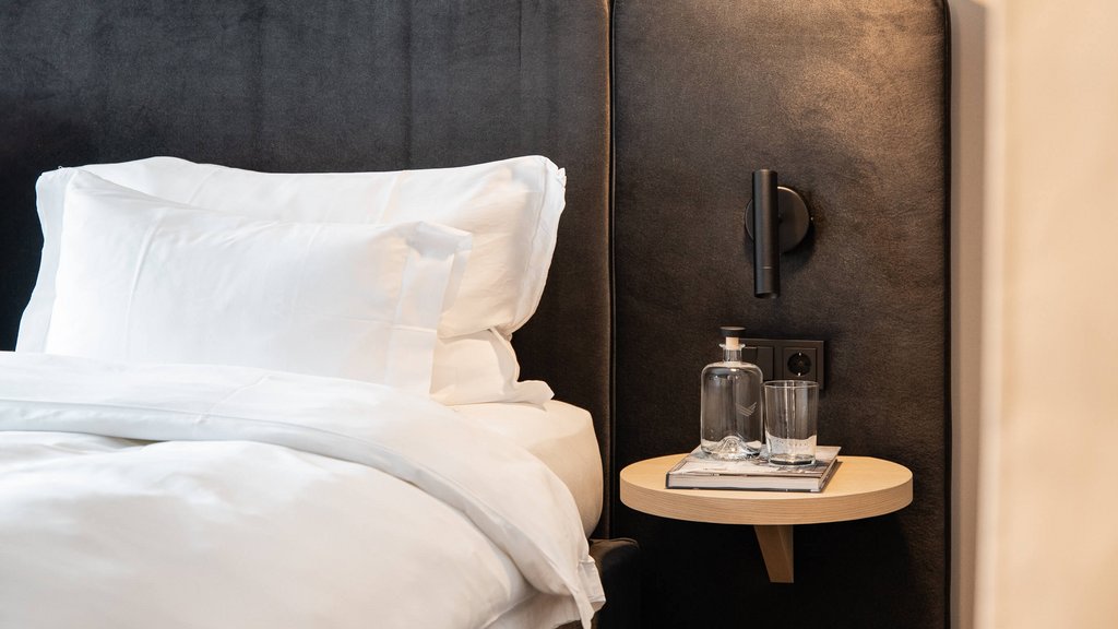 Nahaufnahme eines Bettes mit weißen Kissen und kleinem Beistelltisch mit Wasserflasche