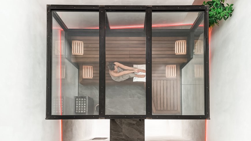 Frau in Handtuch sitzt in moderner Sauna mit Glasdach und roter LED-Beleuchtung