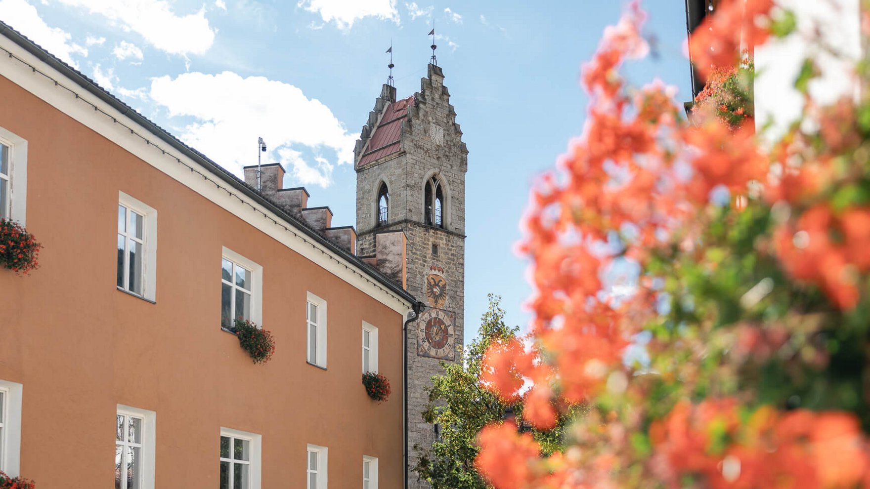 Die perfekte Location für euer Apartment in Sterzing Turm mit Uhr an einem historischen Gebäude neben einem orangen Haus mit Blumen an Fenstern