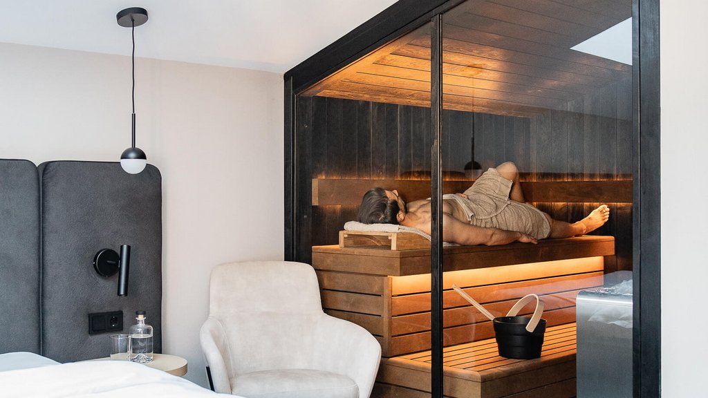 Person entspannt in Sauna neben modernem Schlafzimmer mit weißem Bett