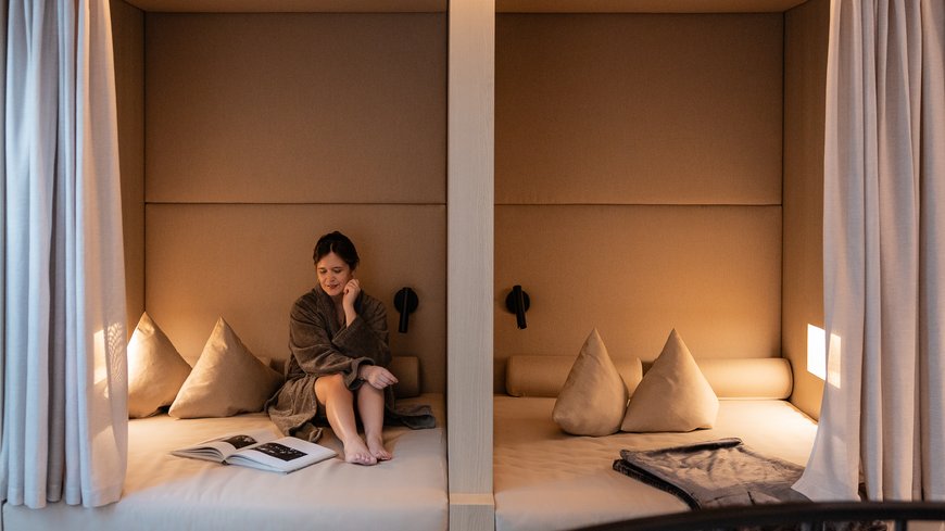 Benessere all’Aquila Nera Donna in accappatoio seduta in nicchie beige con libri e cuscini