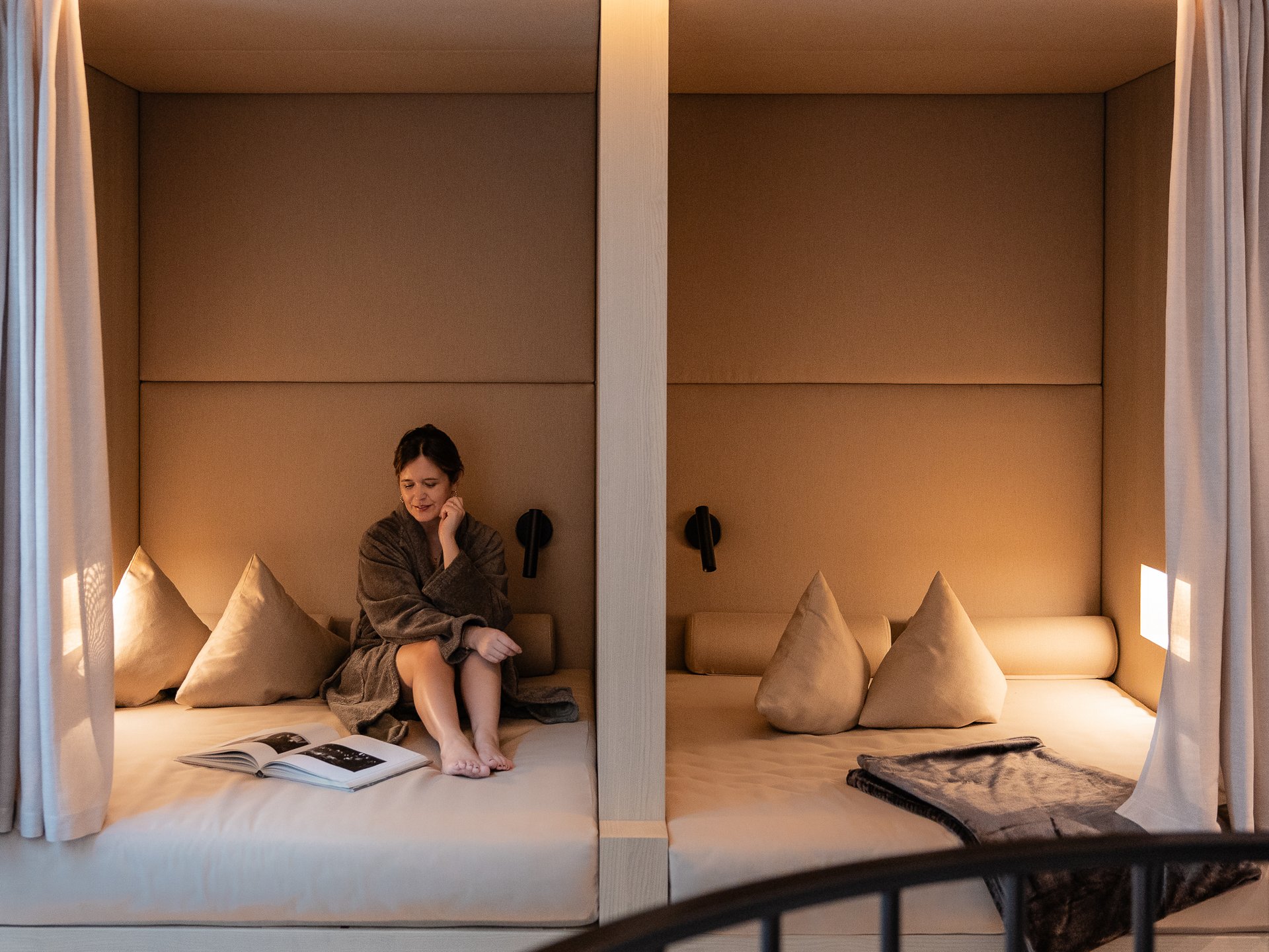 Woman in bathrobe sitting in cozy beige niches with books and pillows