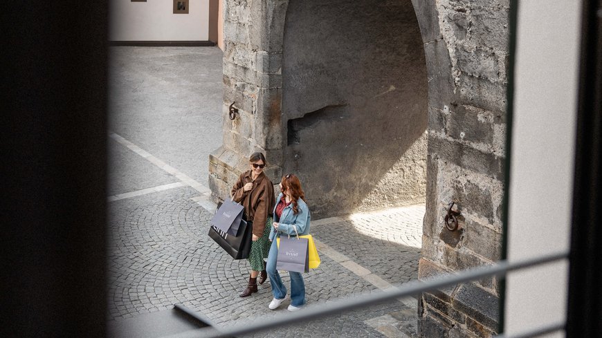The laid-back town on the Isarco/Eisack river Two women carrying shopping bags walk through a stone archway