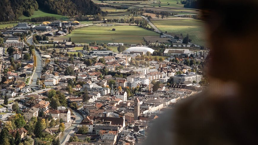 Die perfekte Location für euer Apartment in Sterzing Blick auf eine Alpenstadt mit Bergen und Feldern, Person im Vordergrund unscharf