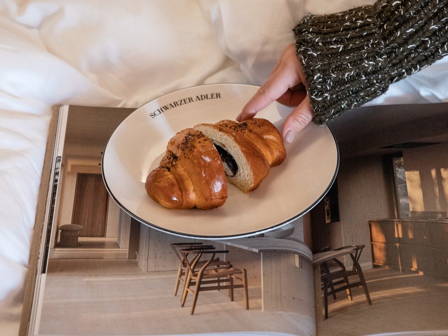 Charmantes Boutique Hotel in Sterzing Hand nimmt Croissant auf Teller auf Bett mit offenem Magazin