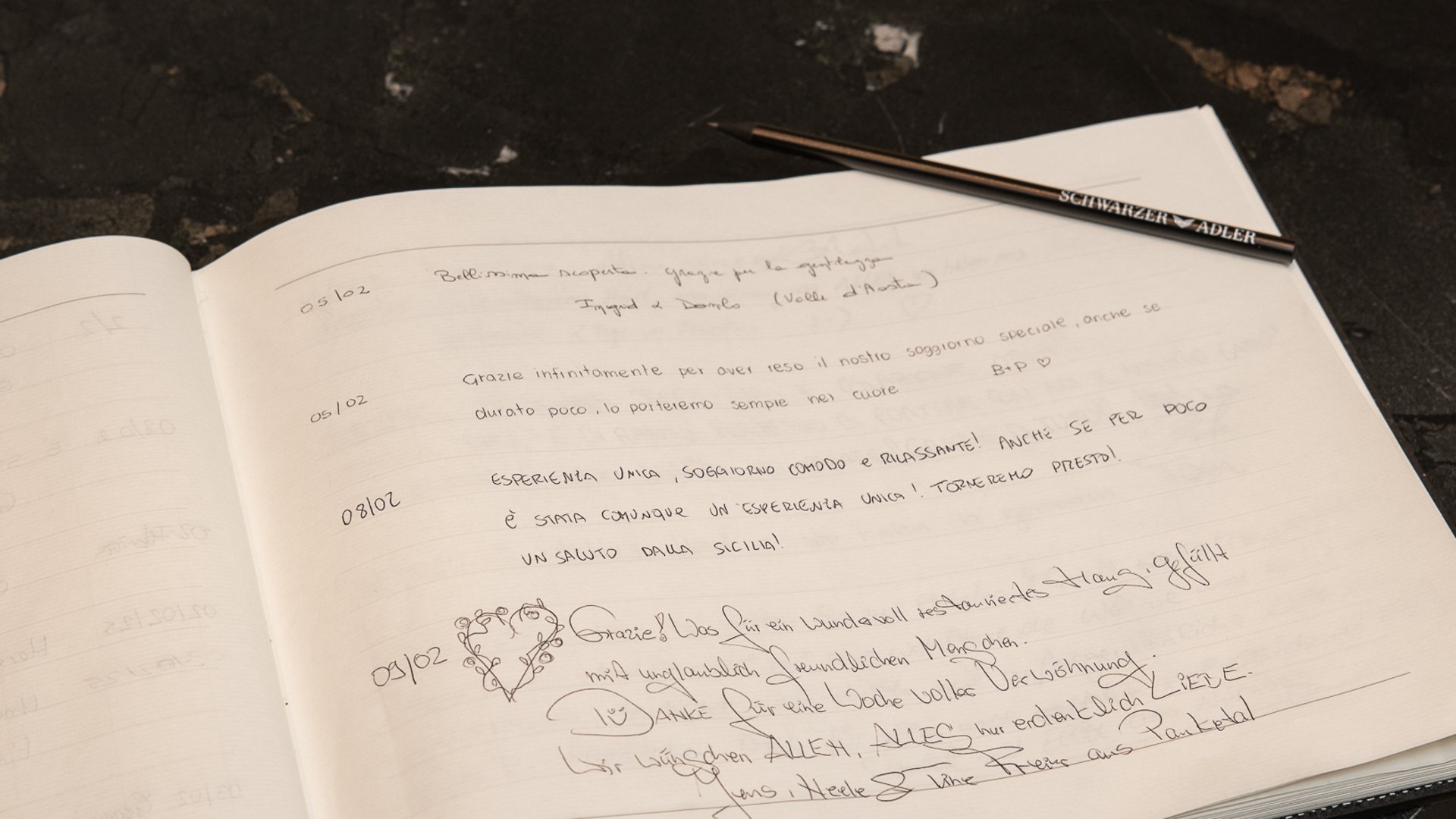 Open guestbook with handwritten messages and pen on dark table