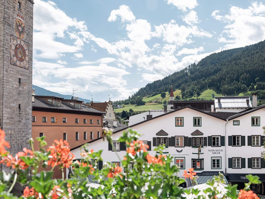 Aquila Nera: la storia del nostro albergo a Vipiteno Vista di un villaggio con torre dell'orologio, fiori e montagne verdi sullo sfondo