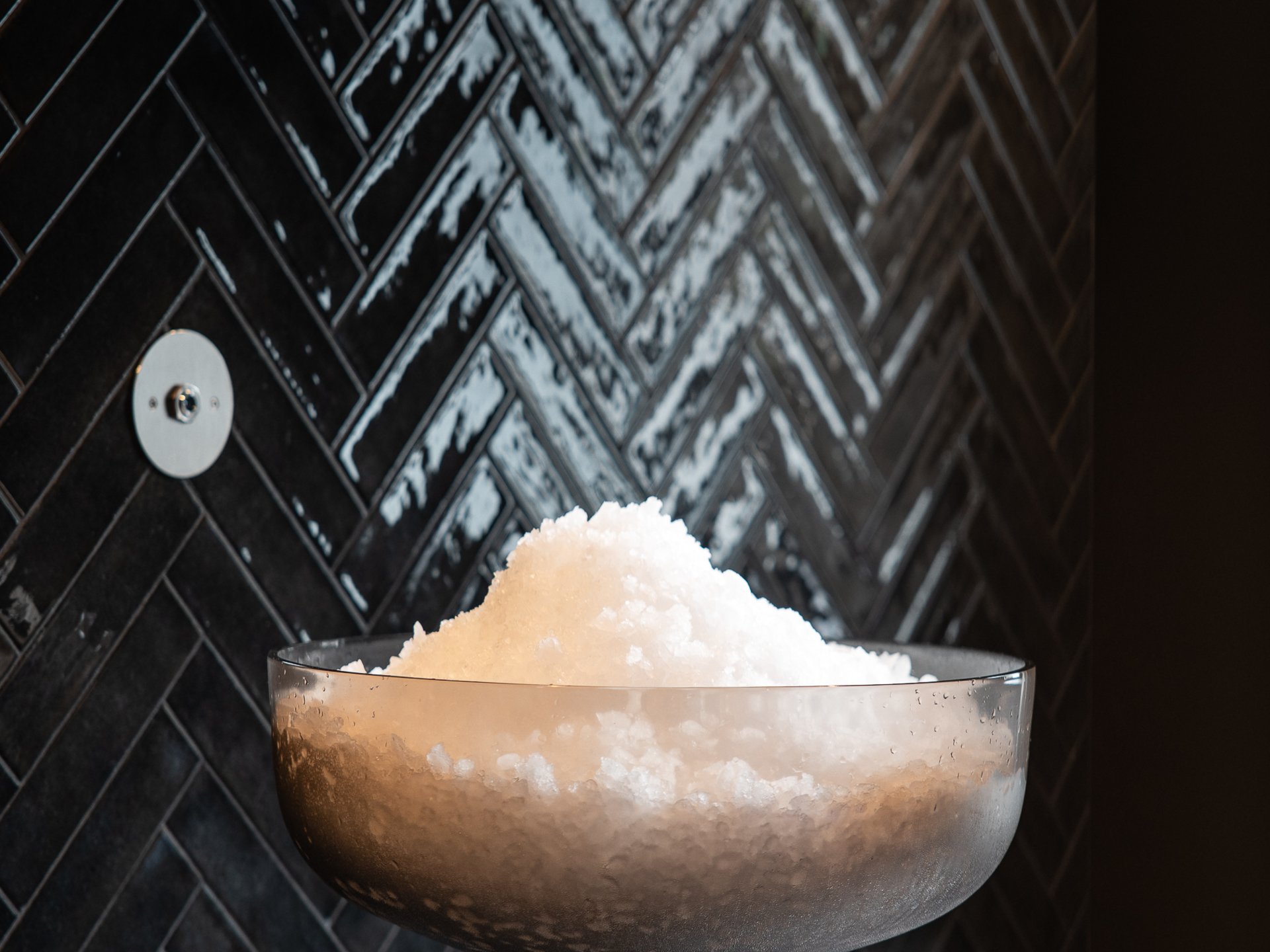 Large bowl of ice in front of black herringbone tile wall