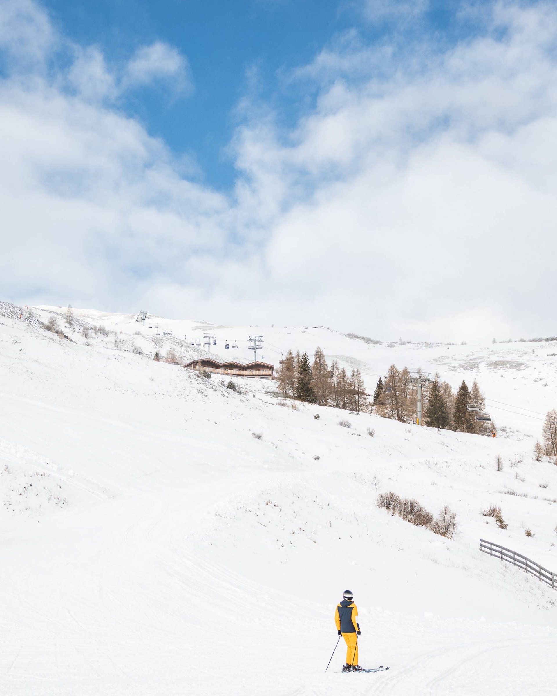 Skifahrer in gelber Kleidung auf verschneiter Piste unter blauem Himmel