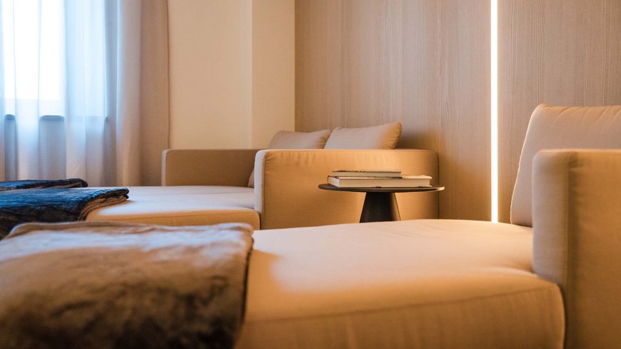 Benessere all’Aquila Nera Soggiorno luminoso con divani beige comodi, coperta e tavolino con libri