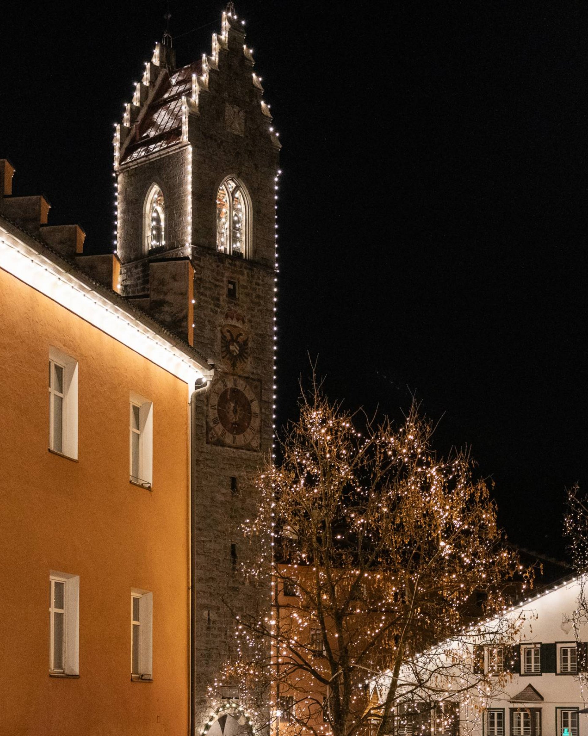 Beleuchteter Kirchturm und Gebäude in der Nacht mit weihnachtlichen Lichterketten