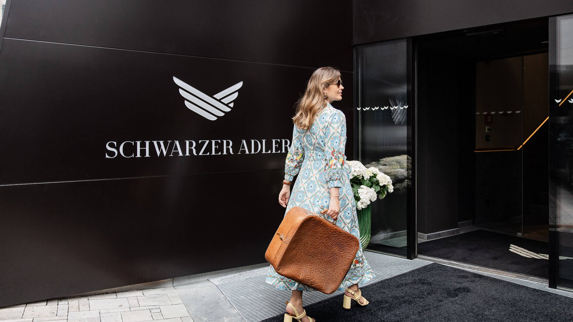 Frau mit braunem Koffer geht ins Hotel Schwarzer Adler