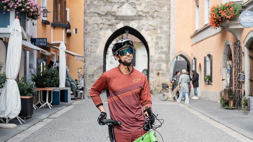 Die perfekte Location für euer Apartment in Sterzing Fahrradfahrer steht mit Mountainbike auf einer Kopfsteinpflasterstraße vor einem historischen Tor