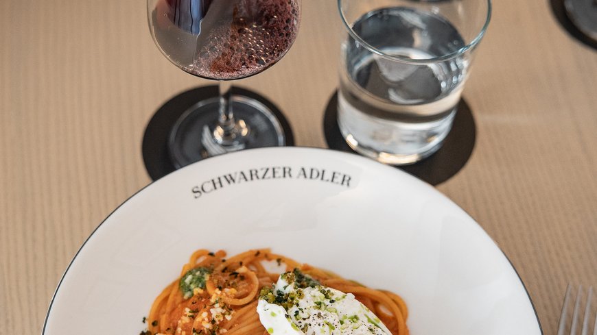 Spaghetti with tomato sauce and burrata, red wine being poured into a glass