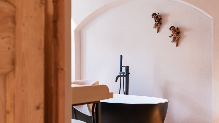 Schwarze Badewanne in hellem Raum mit Holzboden und Deko an der Wand