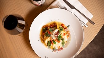 Pasta mit Tomaten, Pesto und Käse auf Teller neben Glas Rotwein