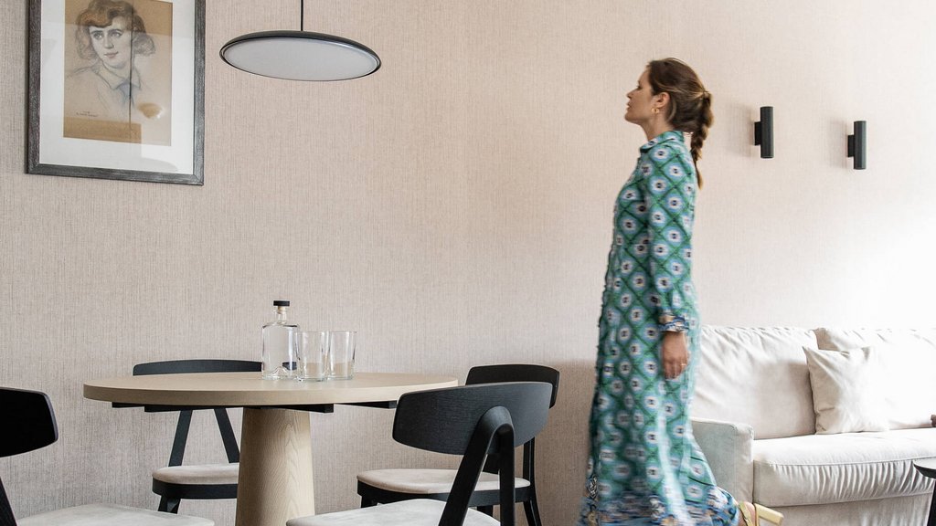 Frau in blauem Kleid geht in modernem Esszimmer mit Holzstuhl und Tisch