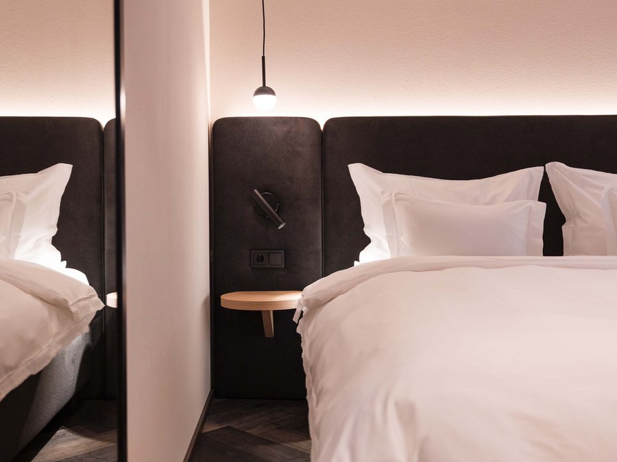 Vacanza a Vipiteno in un hotel sostenibile Camera moderna con biancheria da letto bianca e lampada sospesa