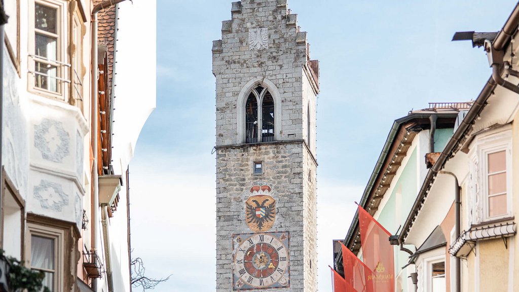 Old clock tower on a street with colorful houses and pale blue sky